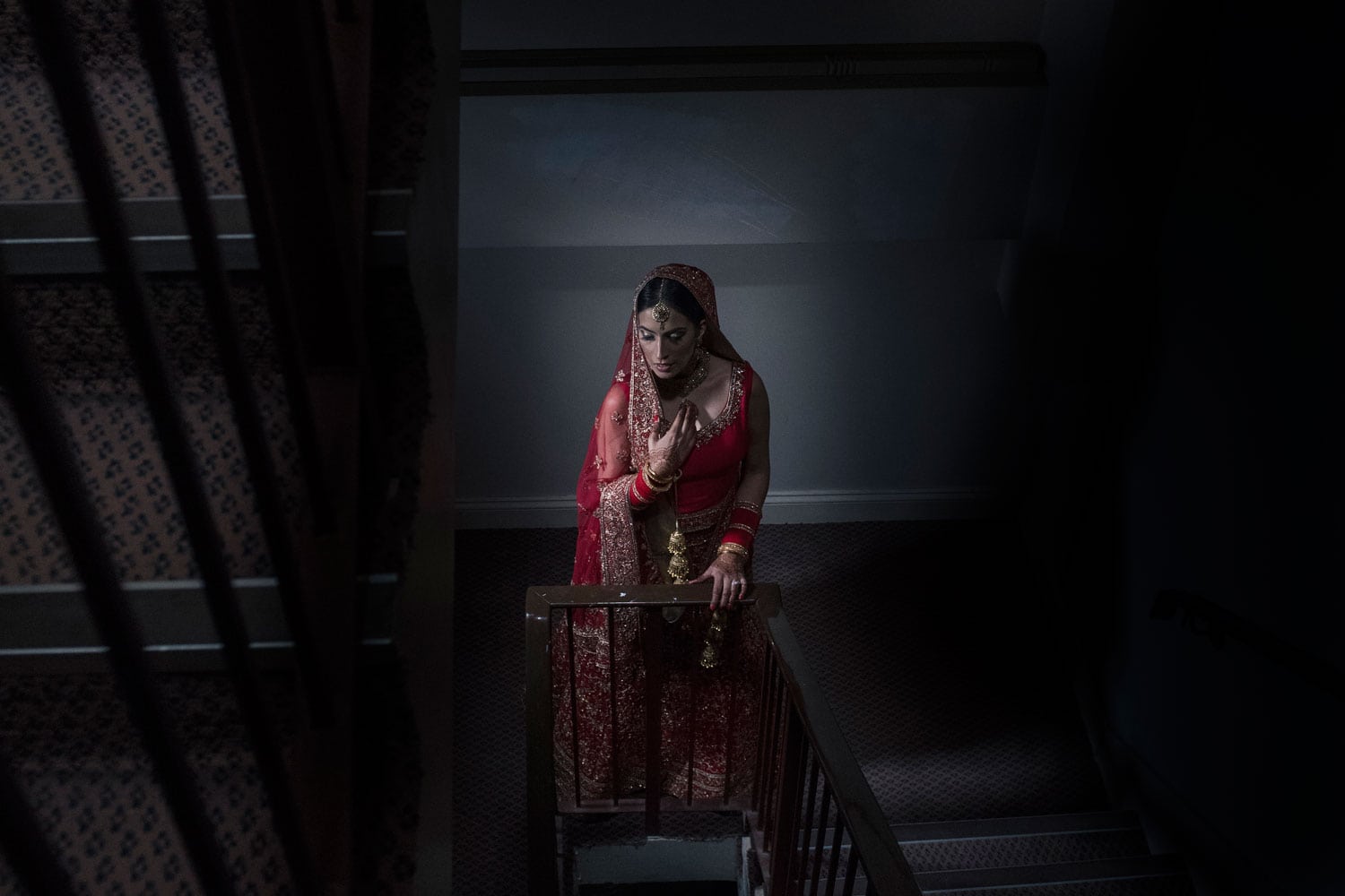 Bride in a red lehenga on a staircase, photographed by East West Photography